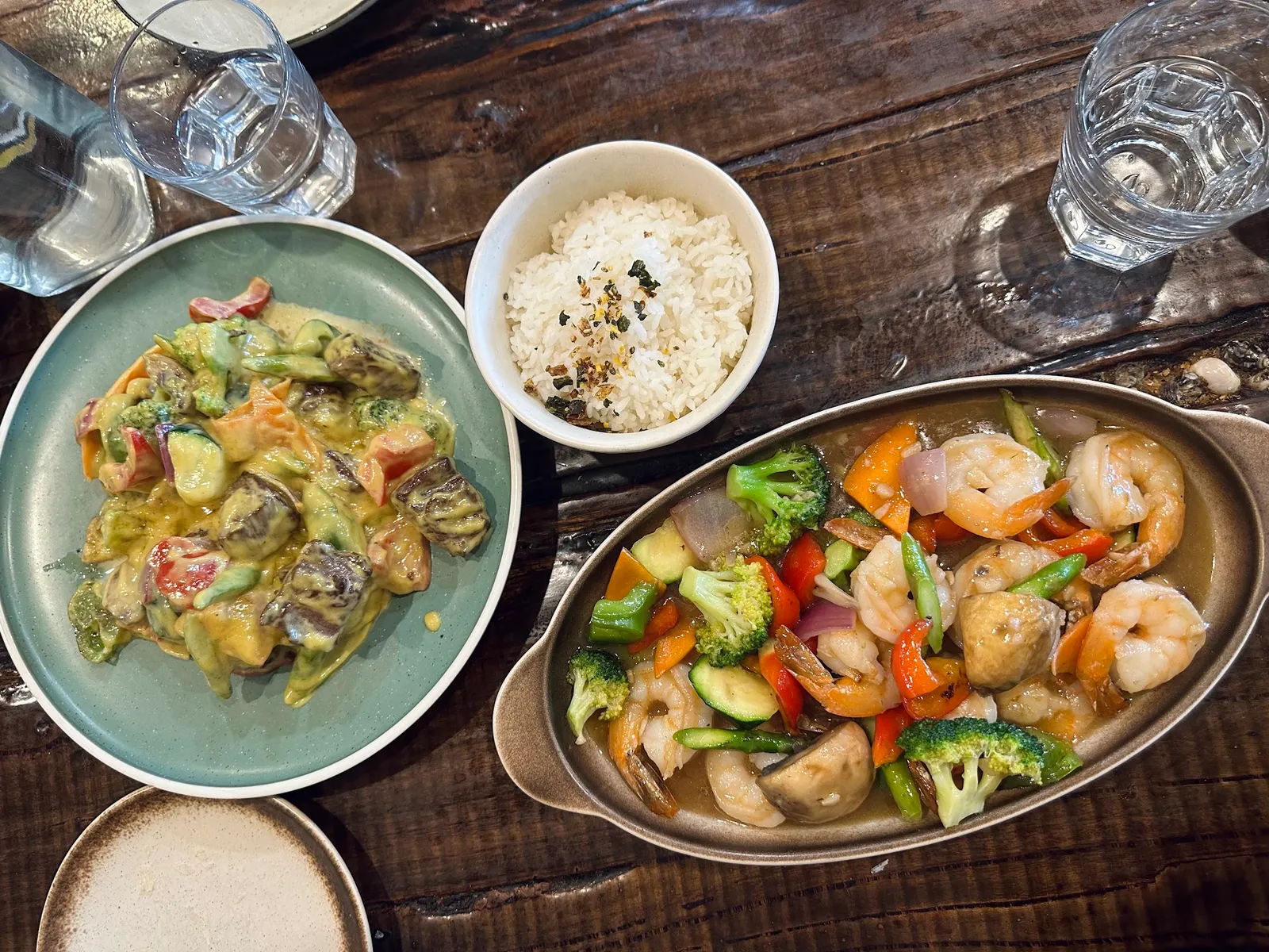 Shared seafood meal with green curry mussels, prawn stir-fry and steamed rice on wooden table
