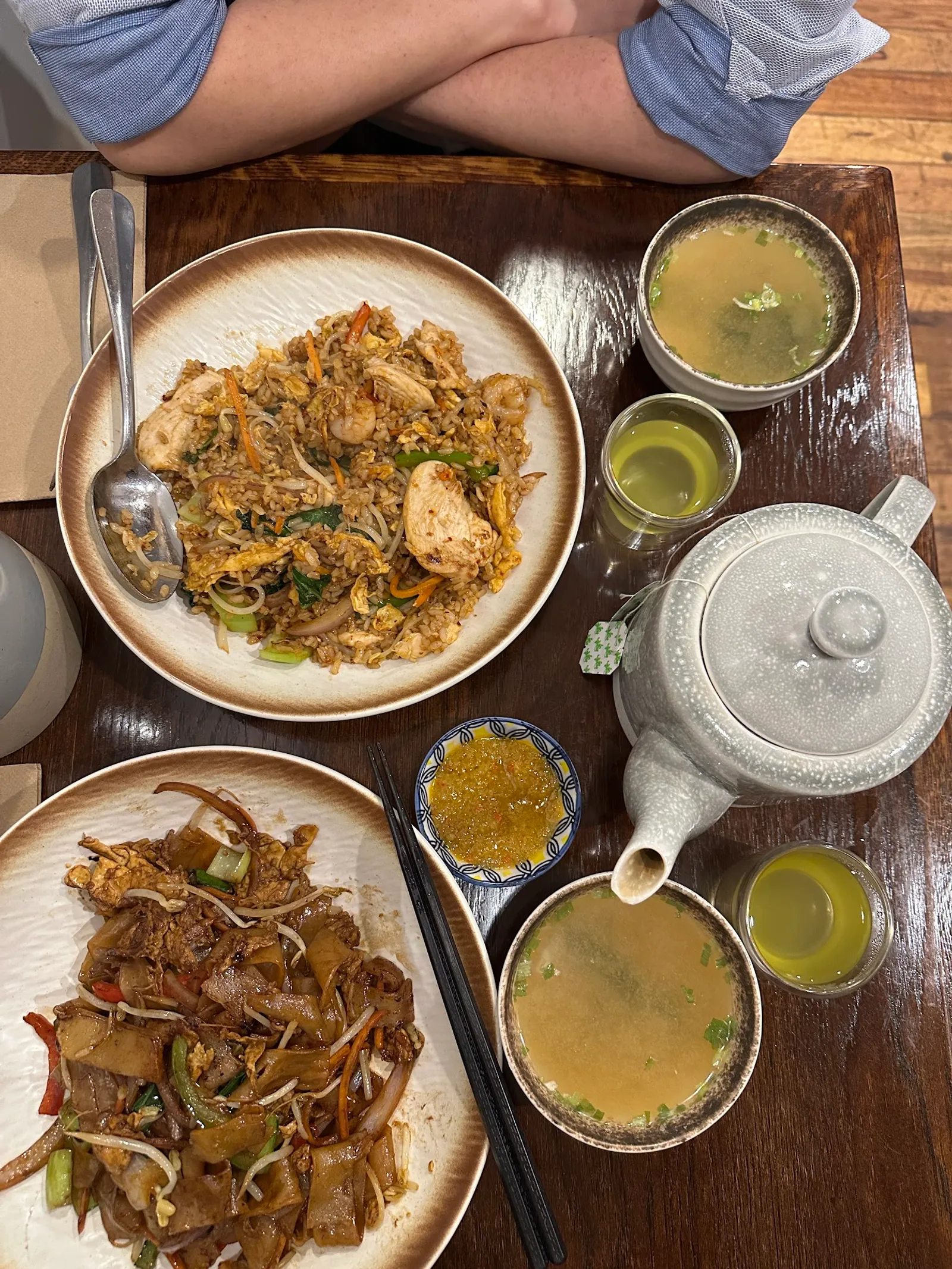 Overhead view of shared Asian noodle dishes with teapot and green tea at restaurant table