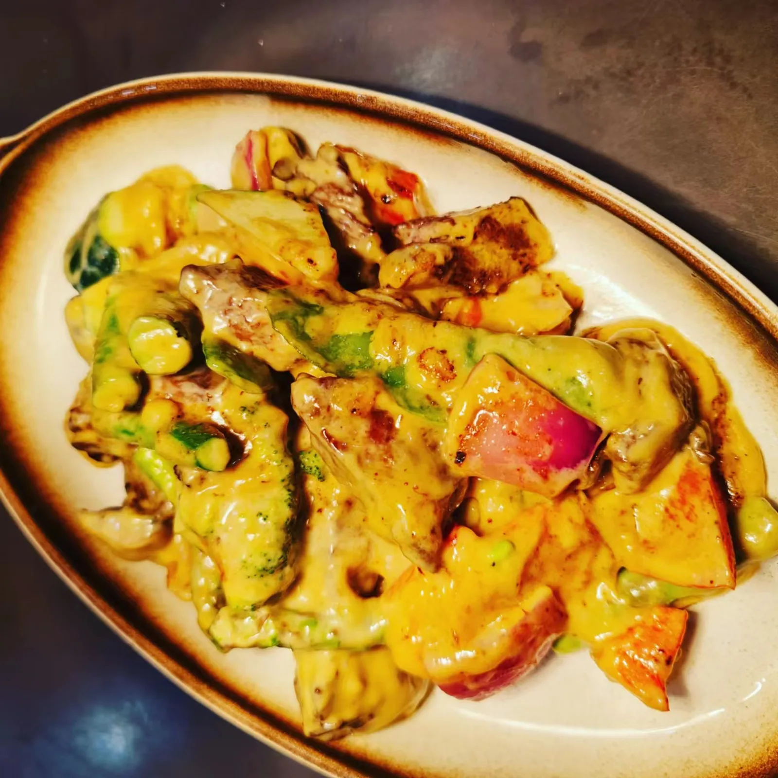Yellow curry with vegetables and seafood in oval ceramic dish on dark counter surface